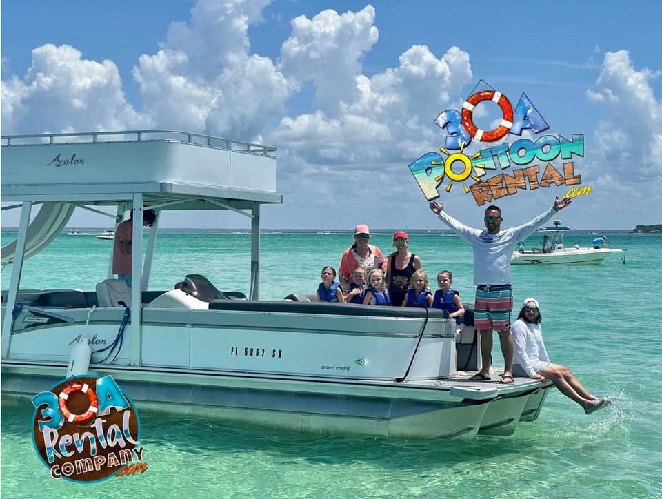 Group of people in life jackets sitting on a silver pontoon boat in clear turquoise water while a smiling man in striped shorts stands on the bow with arms raised, with “30A Pontoon Rental” branding over the bright, cloudy sky.