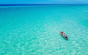 Person lying back and sunbathing on a paddleboard floating alone in crystal-clear, shallow turquoise water that stretches to the horizon under a bright blue sky along Florida’s 30A coast.