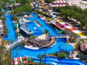 Multiple colorful water slides, including red enclosed tubes and open white and yellow slides, pour into a bright blue pool where guests and lifeguards enjoy a sunny day at Big Kahuna’s waterpark.