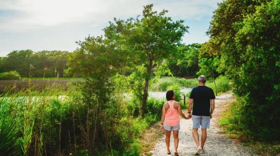 Couple walking hand in hand along a wooded nature trail beside the water at Camp Helen State Park.
