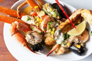 Close-up of a loaded seafood platter with crab legs, shrimp, fish, mussels, corn, and lemon wedges in a creamy butter sauce at Stinky’s Fish Camp.